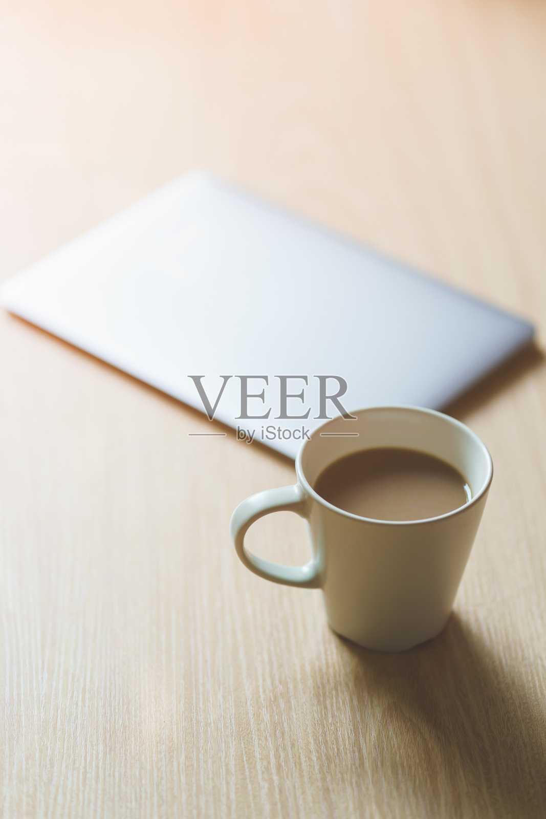 办公桌上有一台笔记本电脑,一杯咖啡,还有早晨的阳光。照片摄影图片