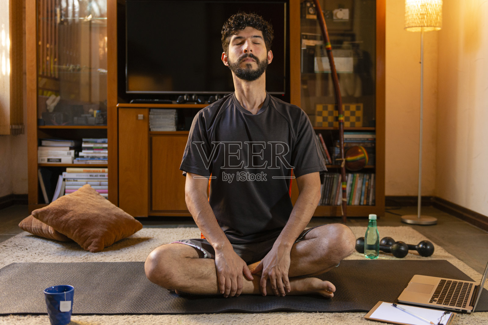 年轻的西班牙裔男子练习呼吸,通过在线老师听课。坐在地毯上。健康做法的概念照片摄影图片