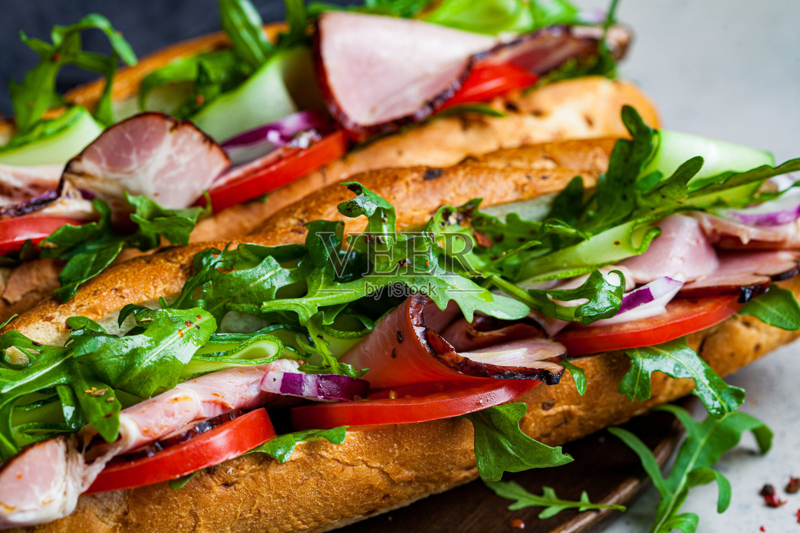 两个新鲜的法棍三明治,肉,番茄,黄瓜和芝麻菜在灰色的背景。照片摄影图片