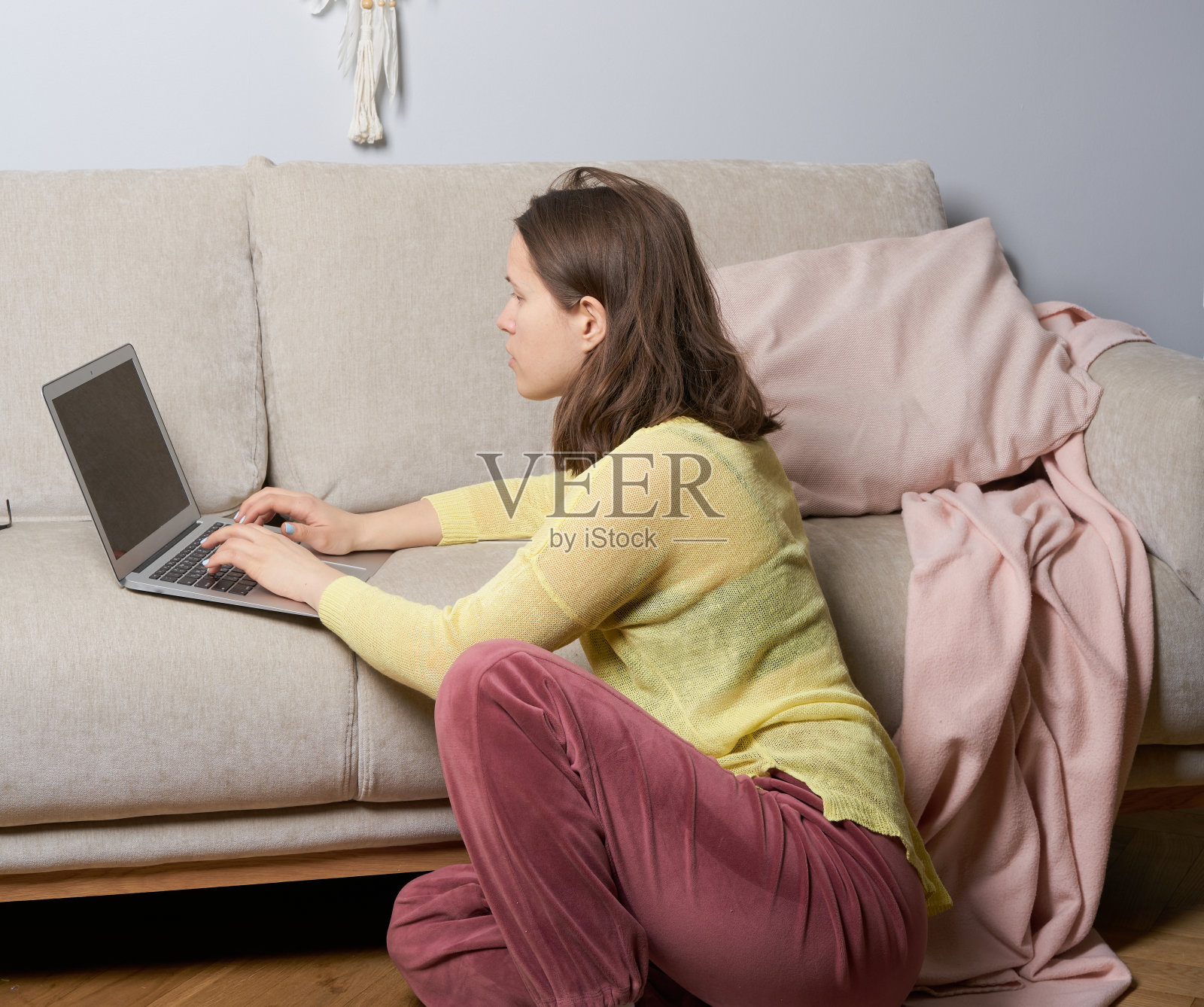 远程工作在家,女性女性在沙发沙发上工作,白天用笔记本电脑,看着屏幕和思考。室内光线波西米亚风格,墙上挂着捕梦网照片摄影图片