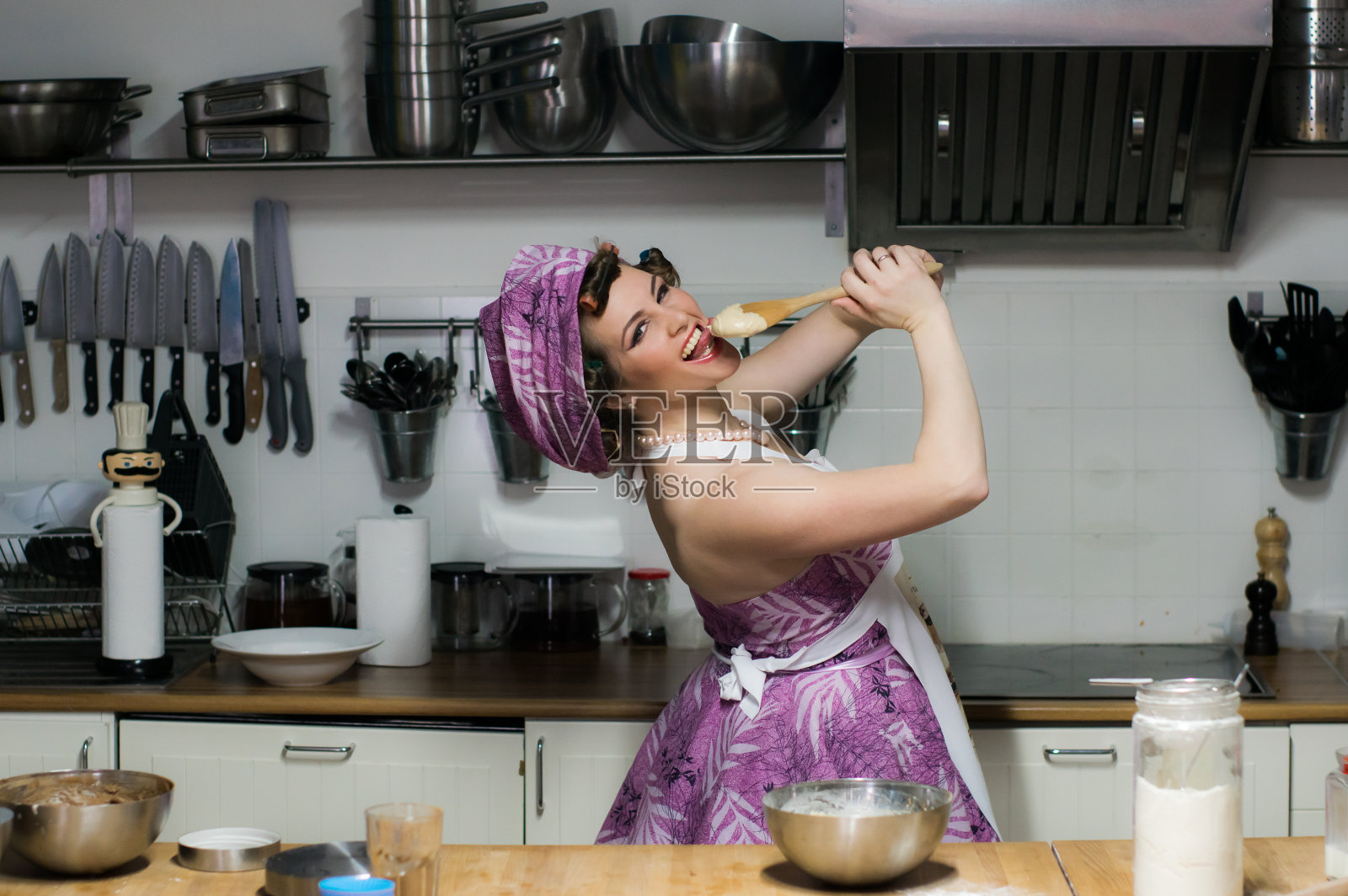美丽的女孩在厨房里做饭,用木勺舀奶油,放在嘴边照片摄影图片