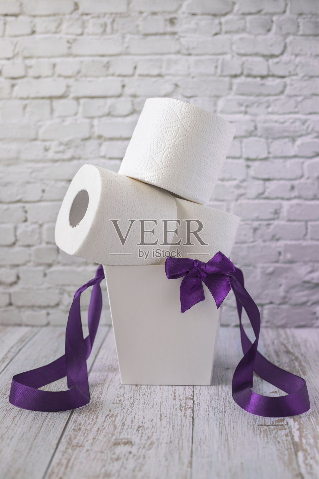 一卷一卷的白色卫生纸放在白色的礼品盒里,上面有紫色的丝带和蝴蝶结,垂直摆放照片摄影图片