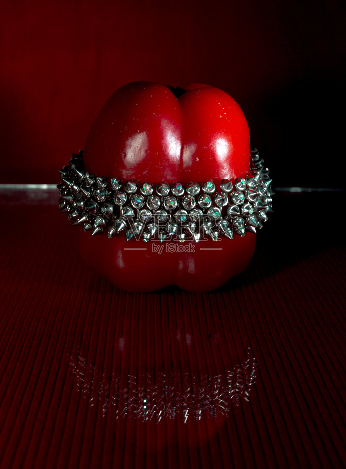 红色灯笼椒上佩戴着一个不寻常的钻石手镯。反射在玻璃上。红色的背景照片摄影图片