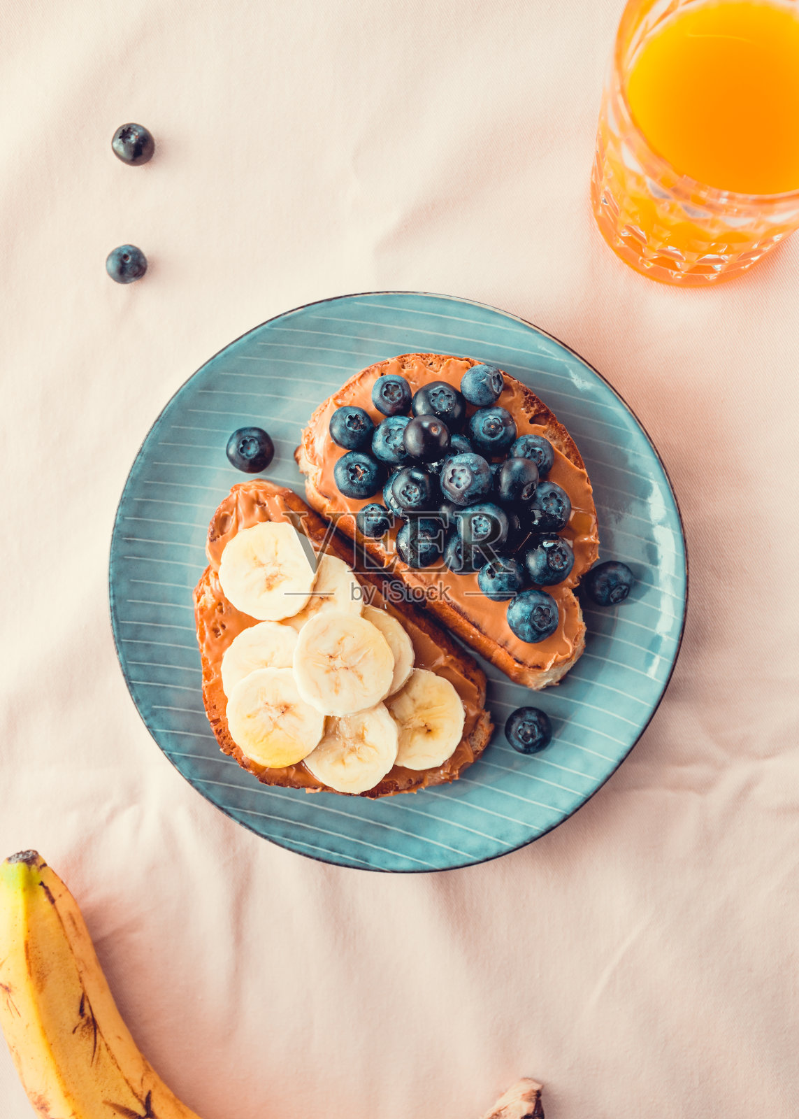 两份涂有花生酱、蓝莓和香蕉的吐司,放在蓝色的盘子里,背景是粉红色的。照片摄影图片