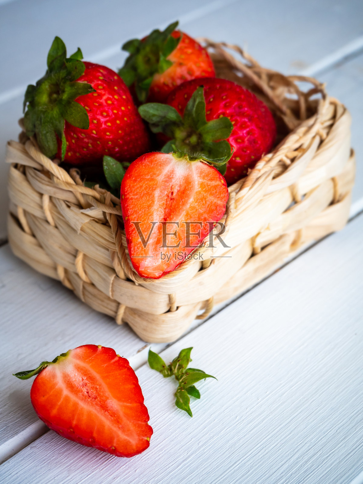 新鲜的草莓放在白色的篮子里,在白色的木桌上切成两半照片摄影图片