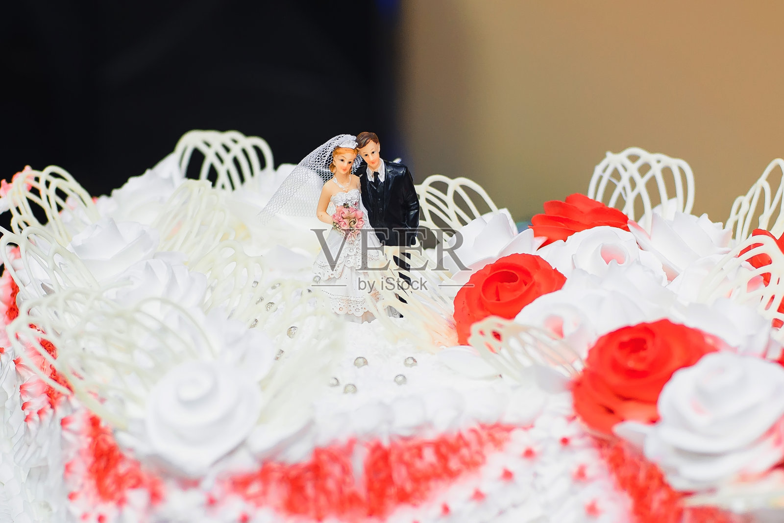婚礼蛋糕用白色奶油装饰,红玫瑰上有新娘和新郎的塑像照片摄影图片