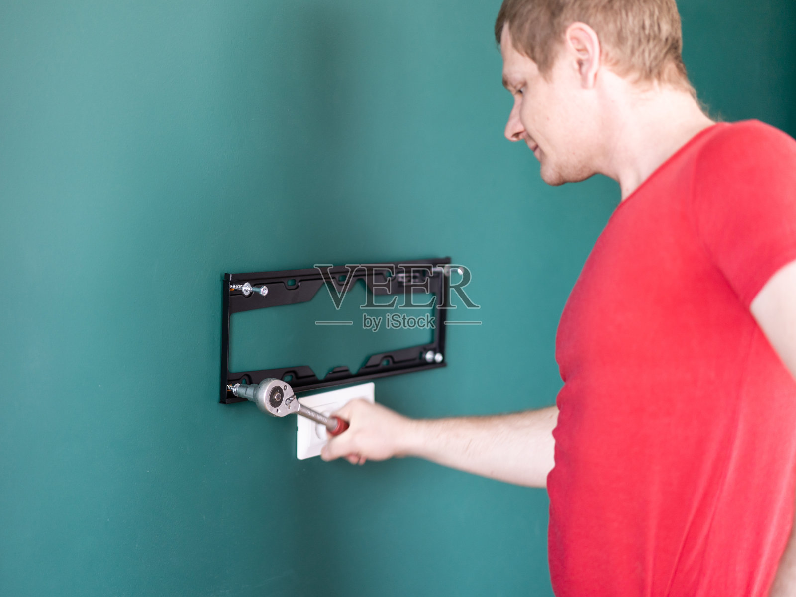 维修和装饰。“一个小时的丈夫”服务。一个人把电视支架固定在墙上。照片摄影图片