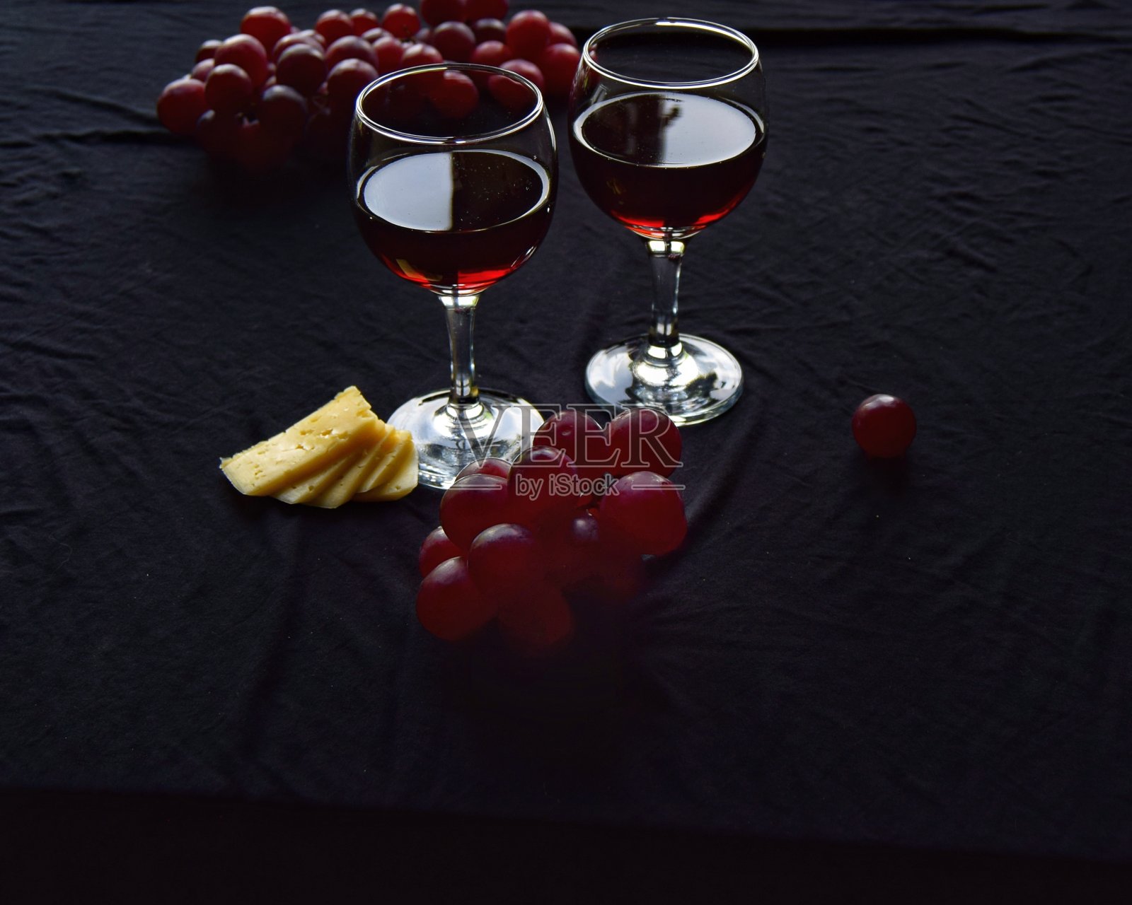 一顿浪漫的晚餐的概念是两杯红酒配上葡萄和奶酪,在黑色的背景下,用深色的钥匙为题字留出空间照片摄影图片