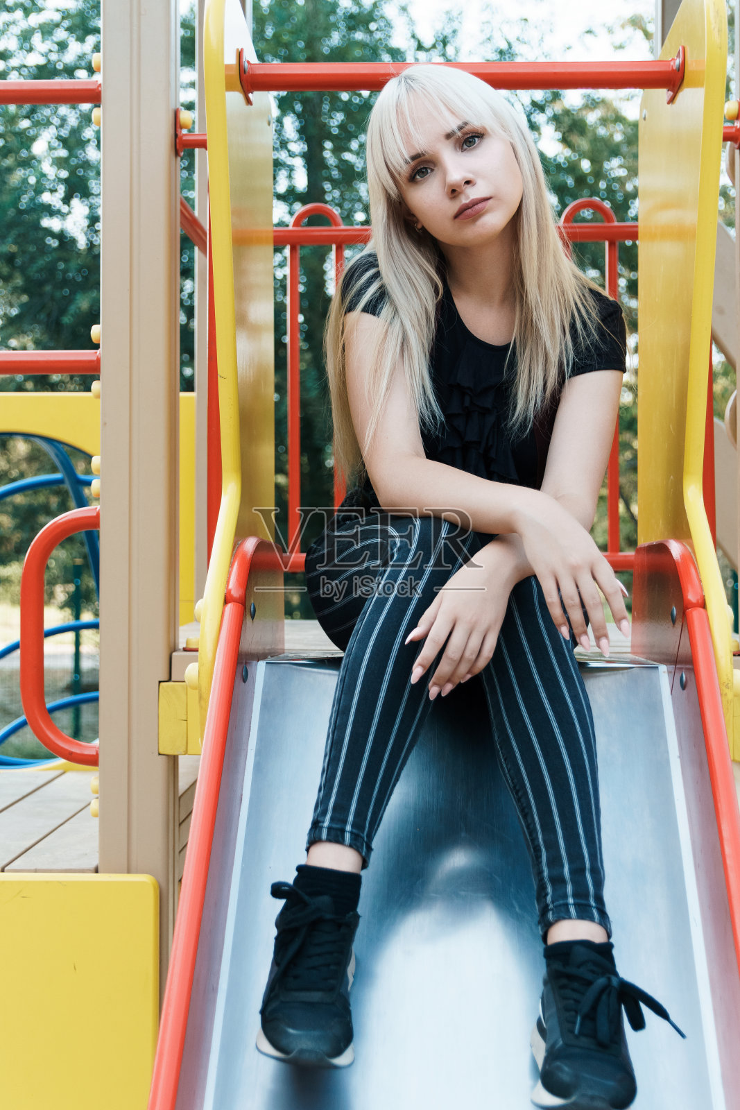 在公园滑梯上,背景模糊的悲伤金发女孩照片摄影图片