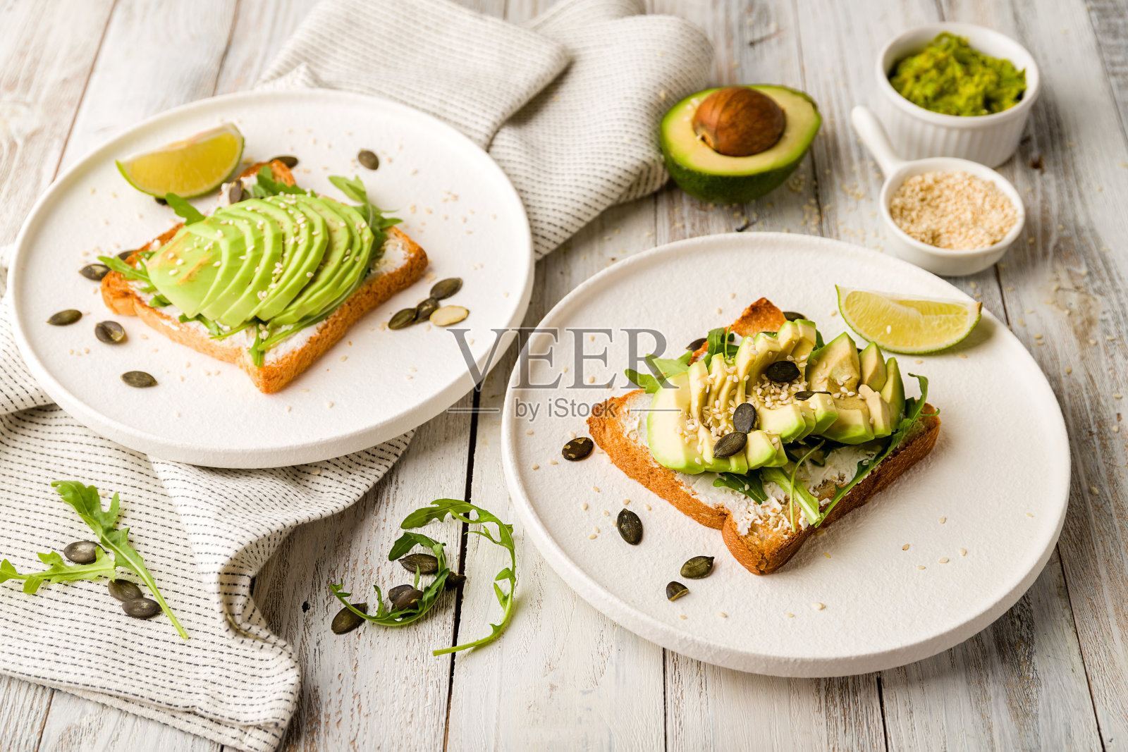 白色木桌上放着牛油果吐司、奶油芝士、鳄梨色拉酱和芝麻菜照片摄影图片