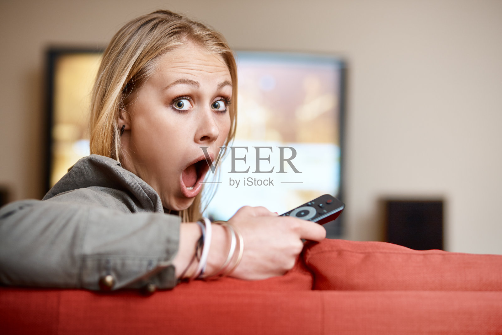 年轻漂亮的金发美女从电视上环顾四周,震惊得喘不过气来照片摄影图片