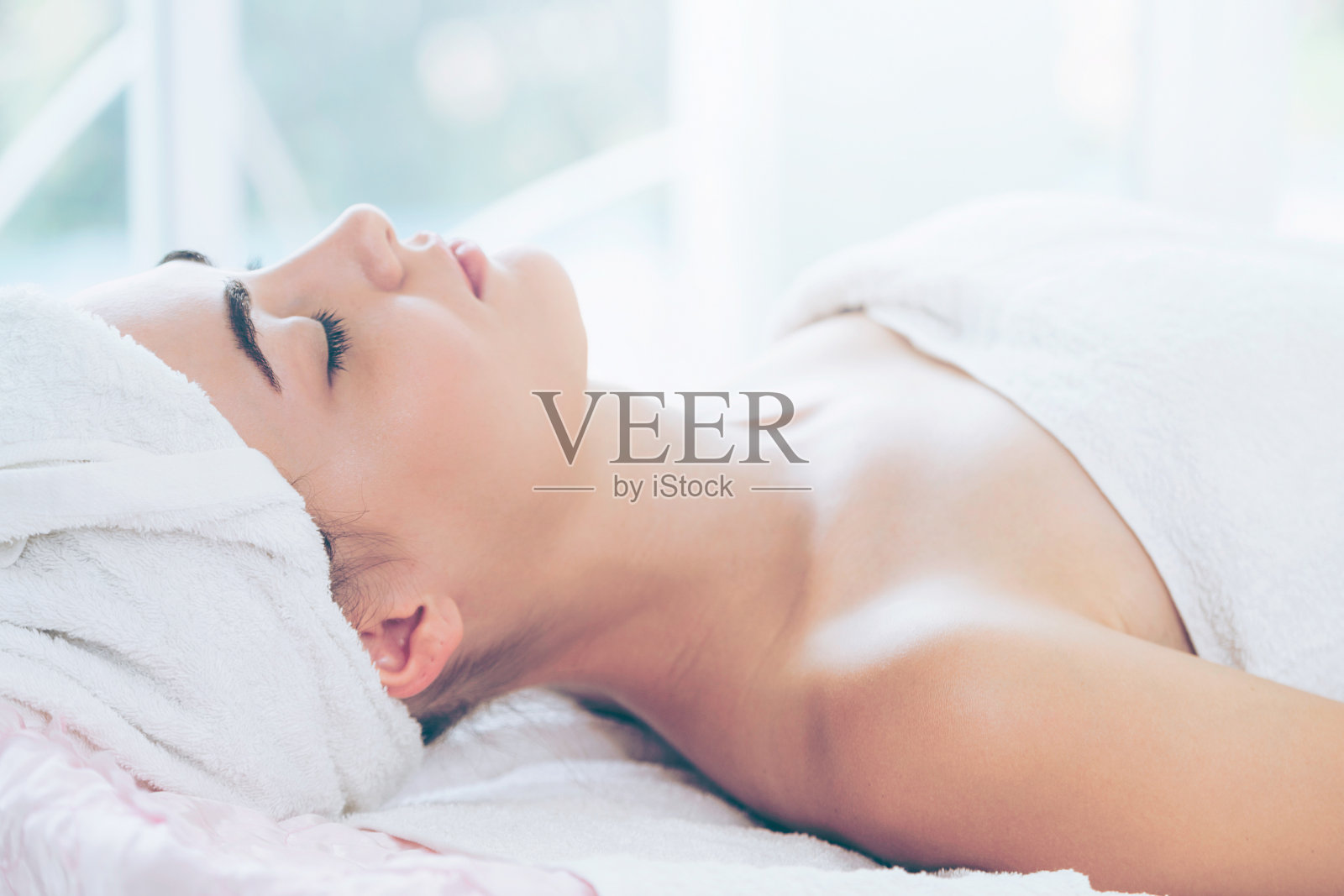 放松的年轻女子躺在水疗床上按摩。照片摄影图片