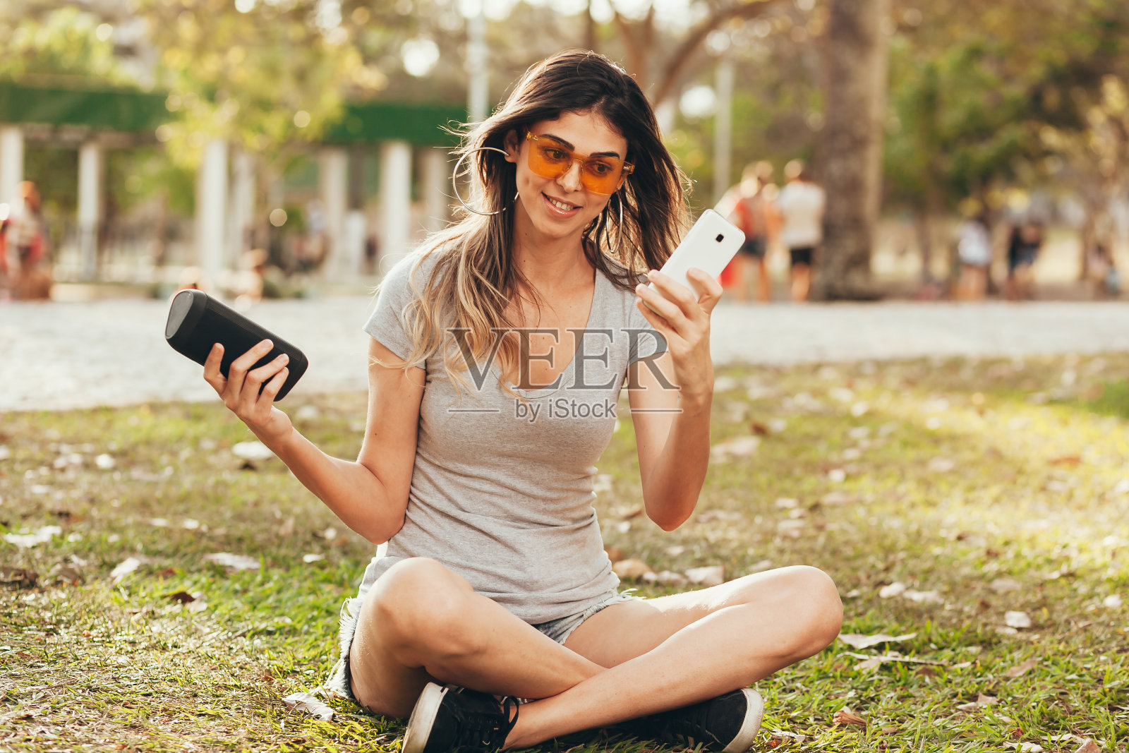 年轻漂亮的女人在户外公园享受音乐。在户外公园用无线扬声器听音乐的女人照片摄影图片