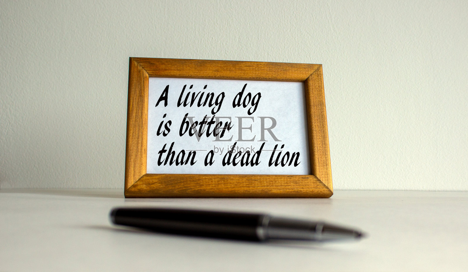 木制的画框,上面刻着“活狗胜过死狮”,上面印着美丽的白色fon。钢笔在桌子上。照片摄影图片