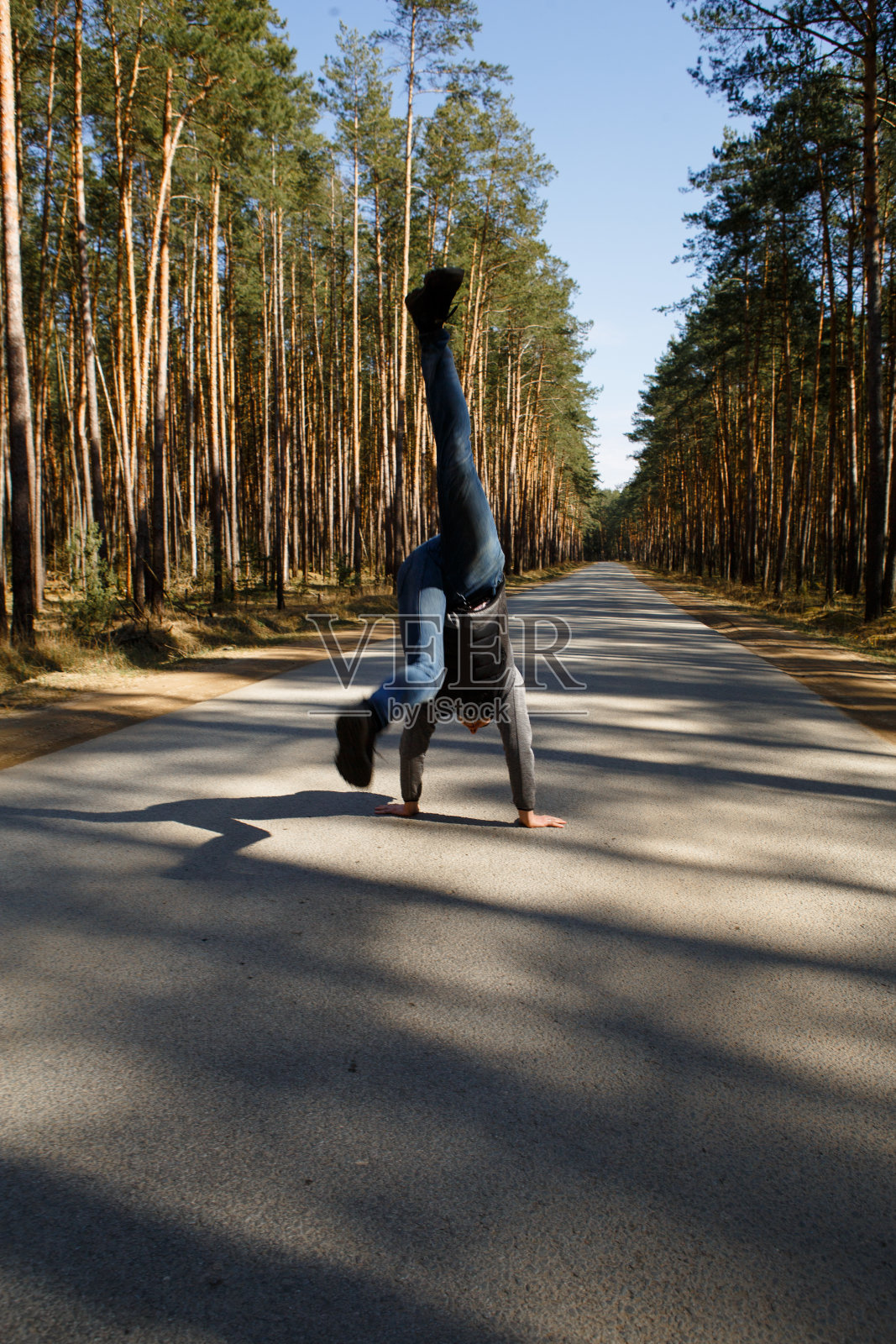 一个年轻人双手倒立在柏油路中间穿过一片松树林。照片摄影图片
