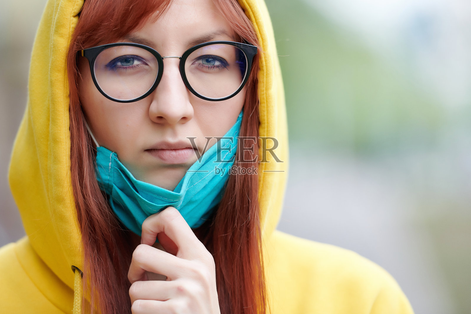 戴着眼镜和兜帽的女孩带着怀疑和愤怒摘下了脸上的医用口罩照片摄影图片
