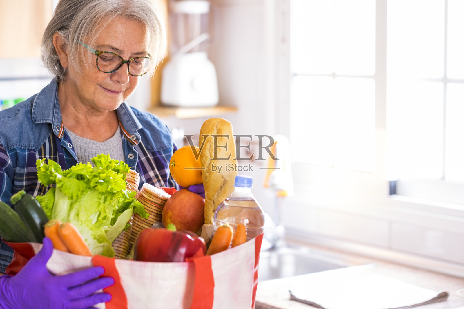 隔离新冠肺炎大流行。戴着防护手套的休闲妇女收到杂货店送货上门的基本必需品。待在家里避免传染的概念照片摄影图片