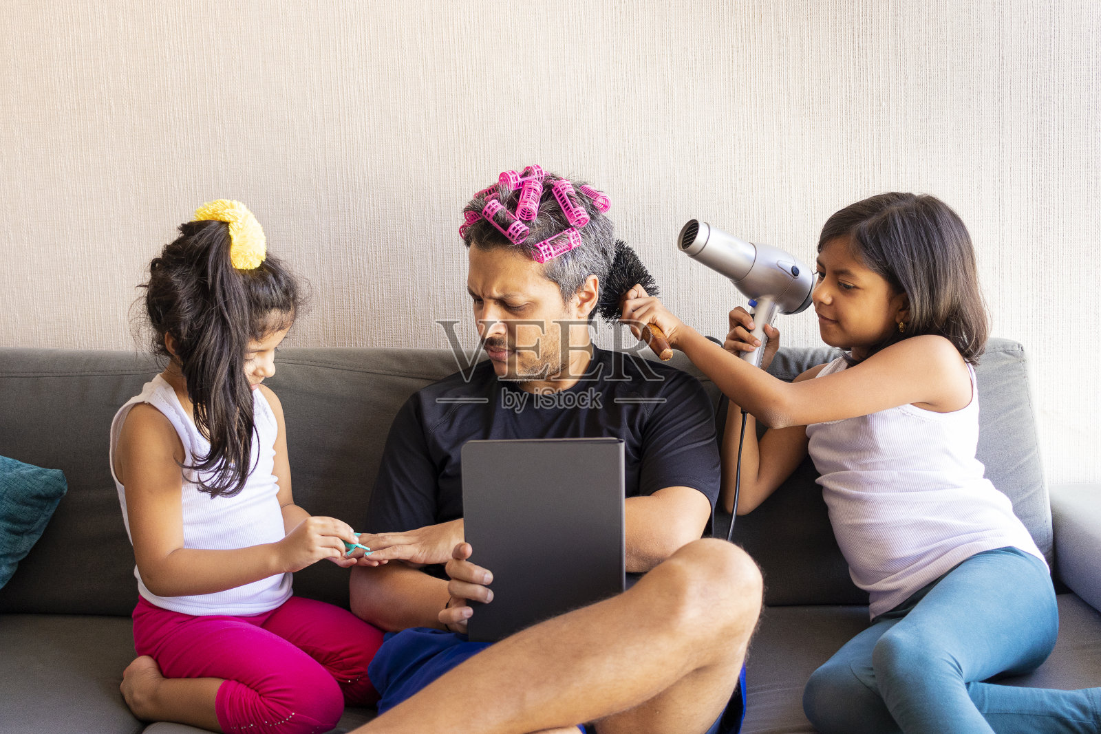 漂亮的女儿们正在给他们年轻英俊的父亲涂指甲、梳理头发照片摄影图片