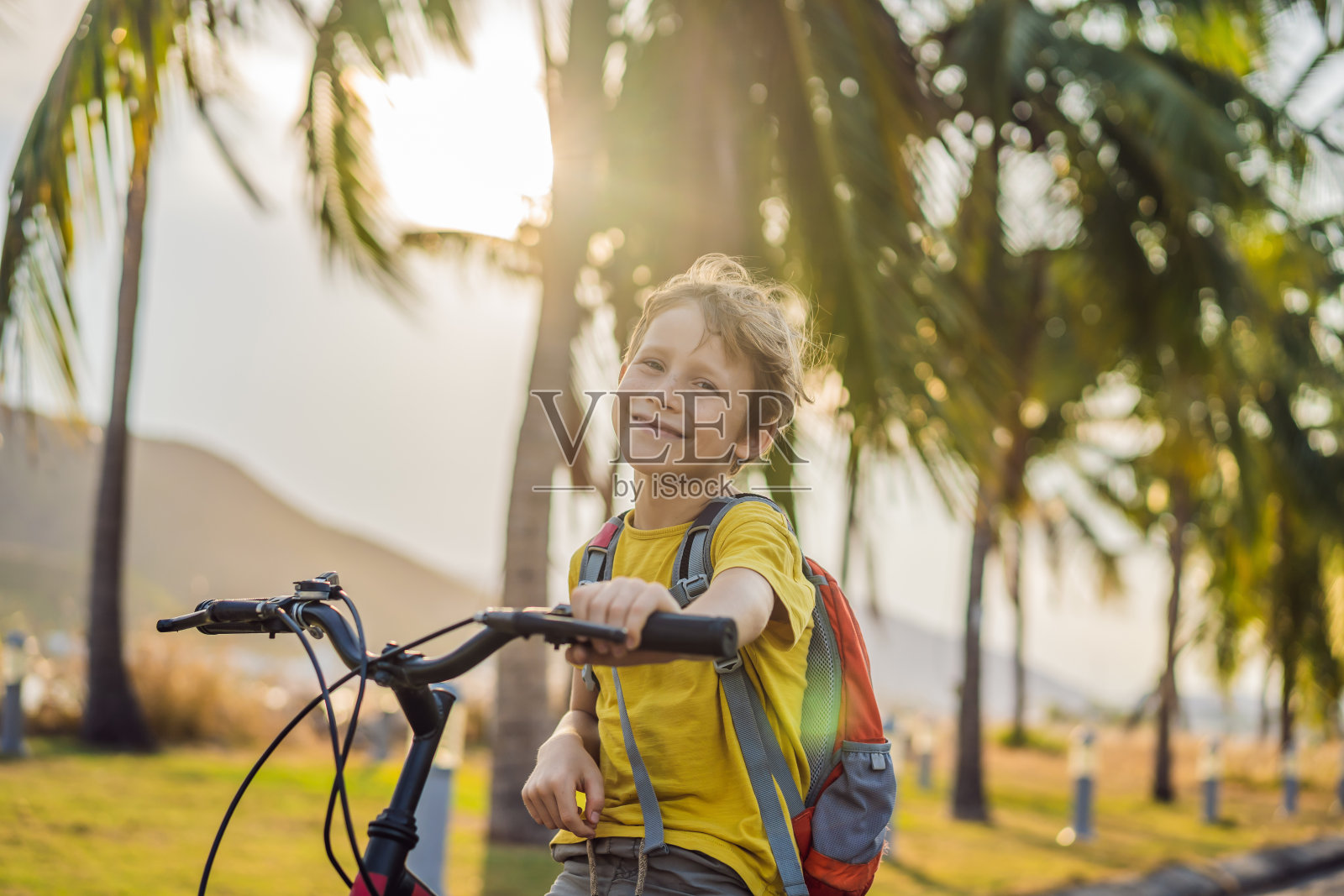 在阳光明媚的日子里,一个活泼的男孩背着背包骑着自行车。快乐的孩子骑着自行车去学校。孩子们在户外上学的安全方式照片摄影图片