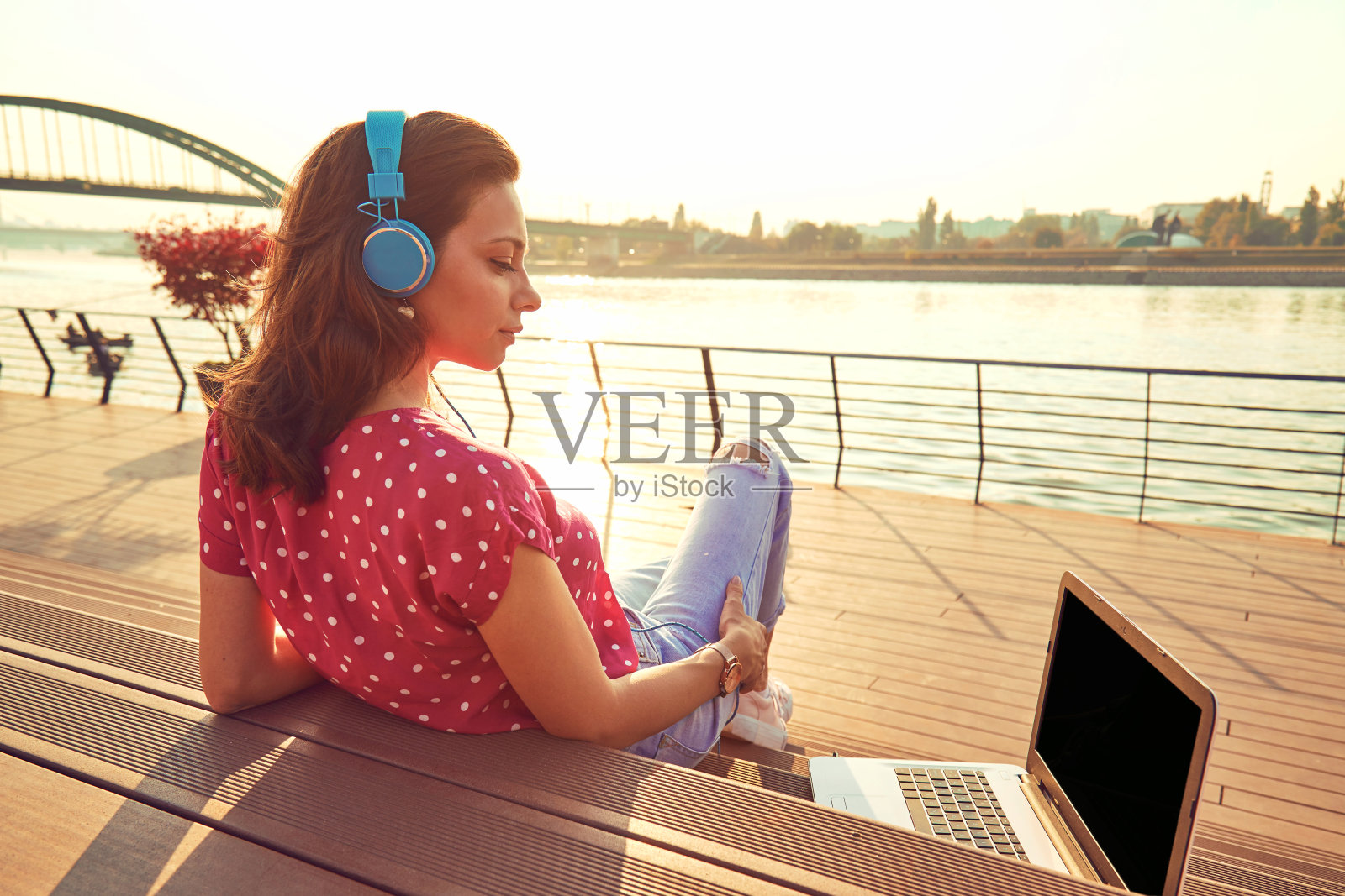 在笔记本电脑上工作,在户外听音乐的漂亮女人。照片摄影图片