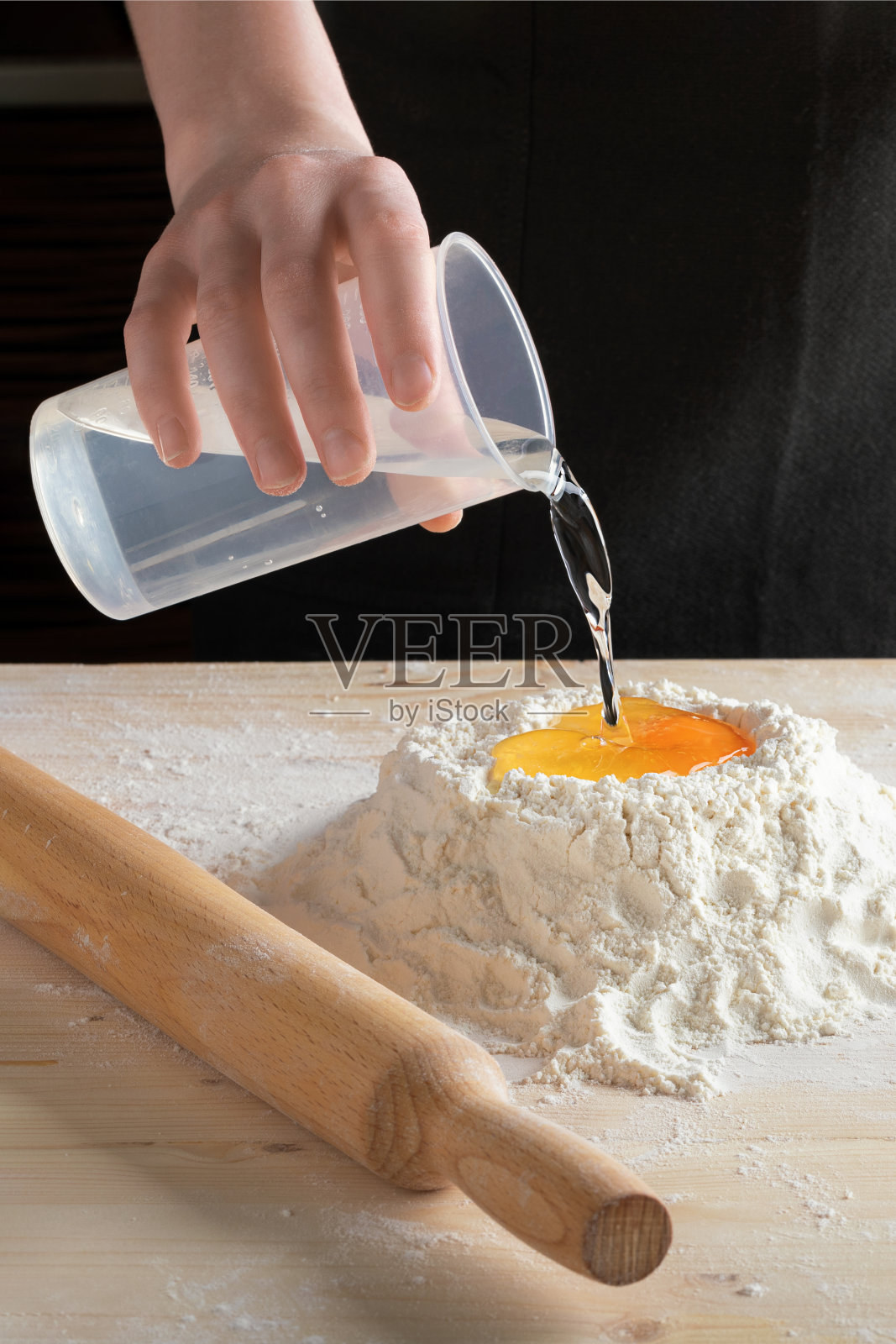 女用手将水和鸡蛋倒入面粉中。照片摄影图片