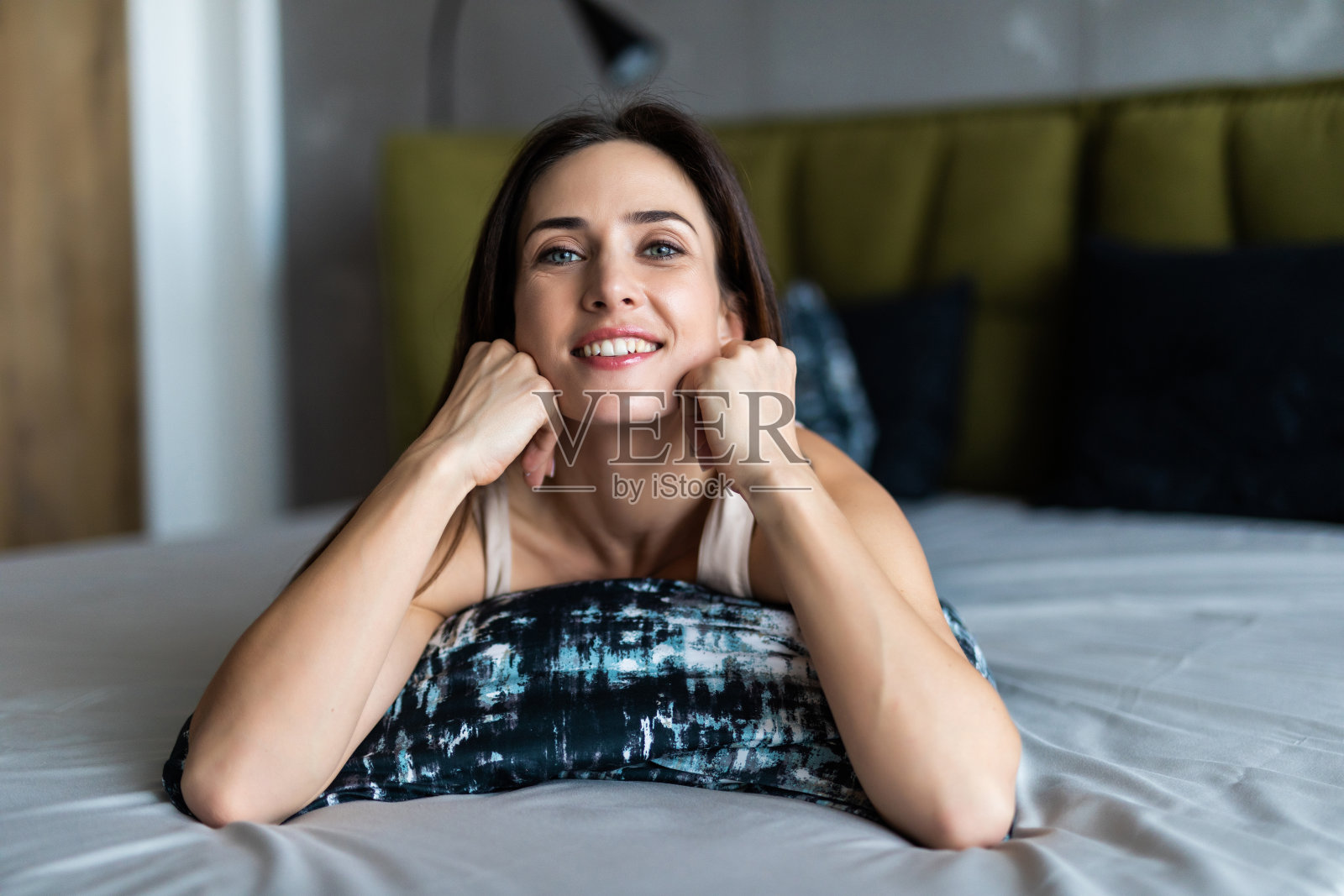 美丽的年轻女子看着相机,而躺在床上在家里照片摄影图片