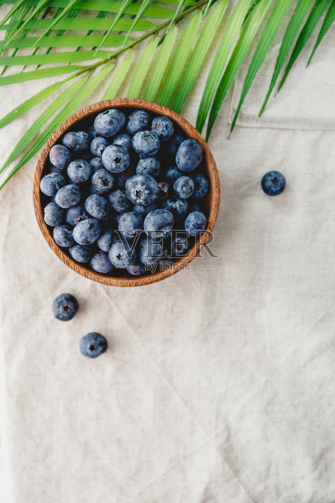 蓝莓装在木碗里,亚麻餐巾上有棕榈叶装饰。环保和夏季背景。照片摄影图片
