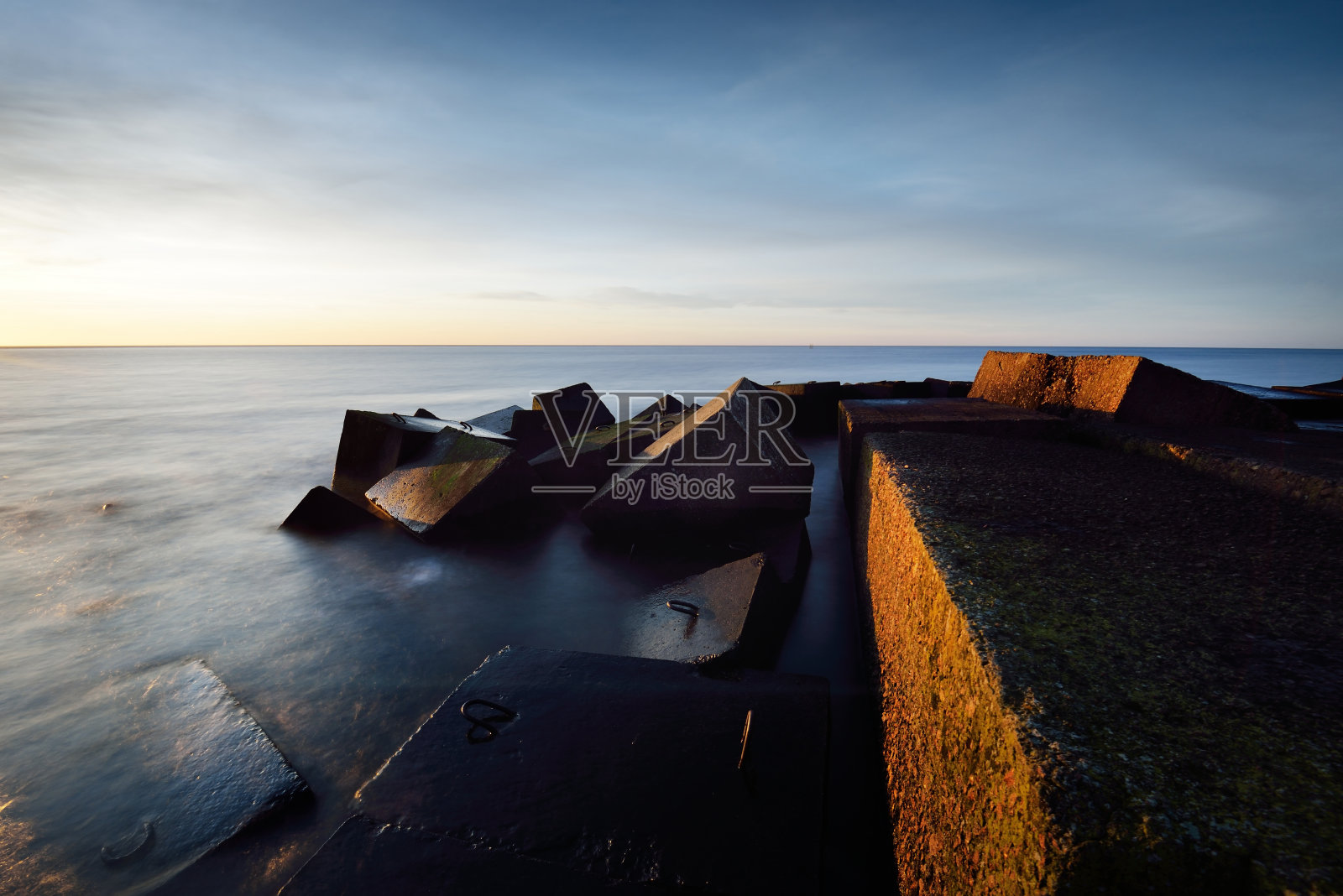 防波堤映衬着缤纷的日落天空。惊人的海景。金色的夕阳透过蓝色的云。长时间的曝光。波罗的海,拉脱维亚里加湾照片摄影图片