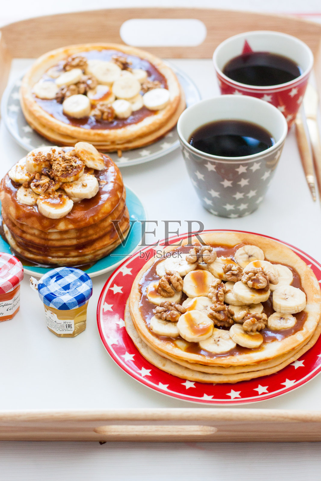早餐托盘有香蕉煎饼,枫糖浆和坚果,一杯咖啡和蜂蜜。照片摄影图片