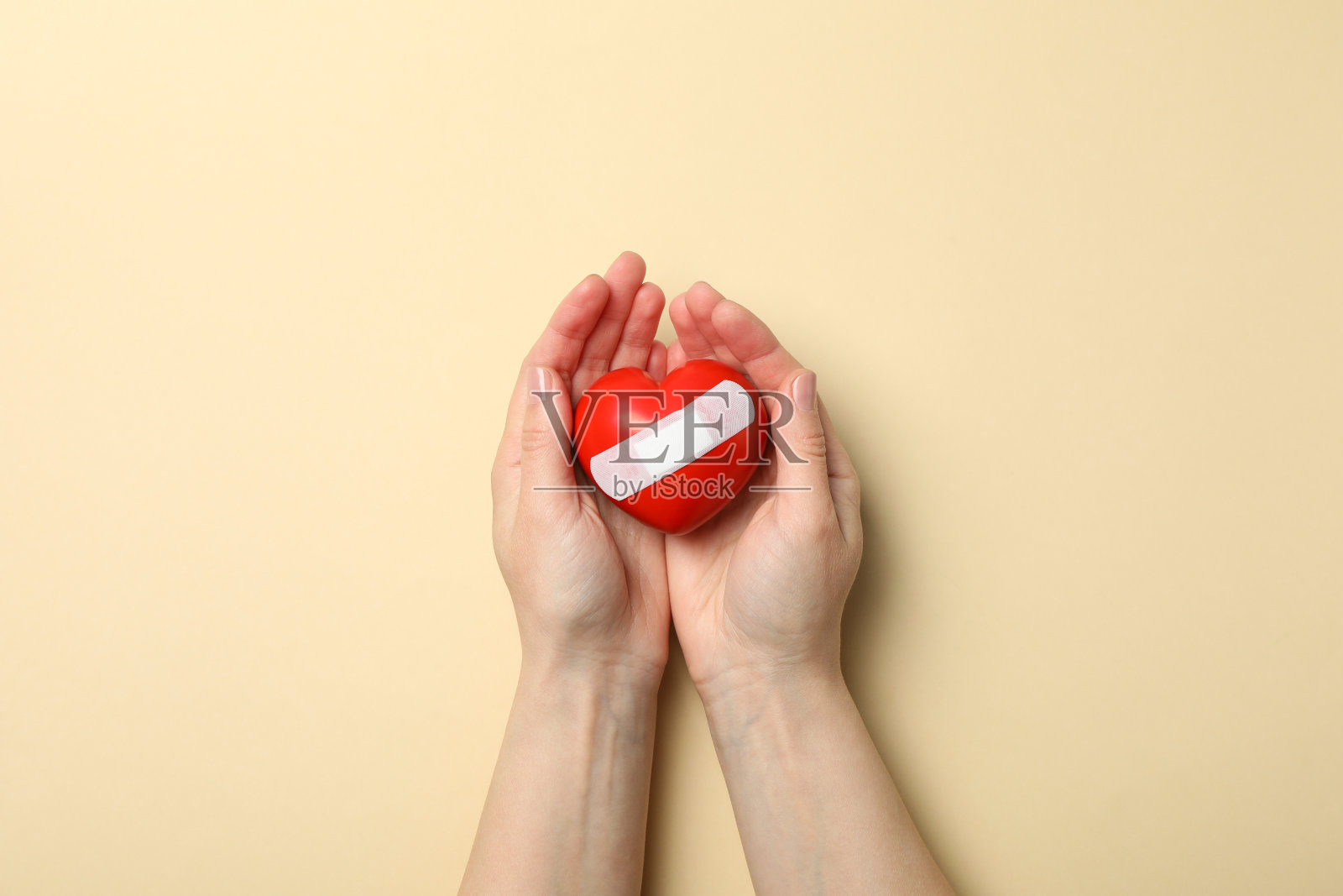 女性双手捧心用胶布贴在米色背景上,俯视图照片摄影图片