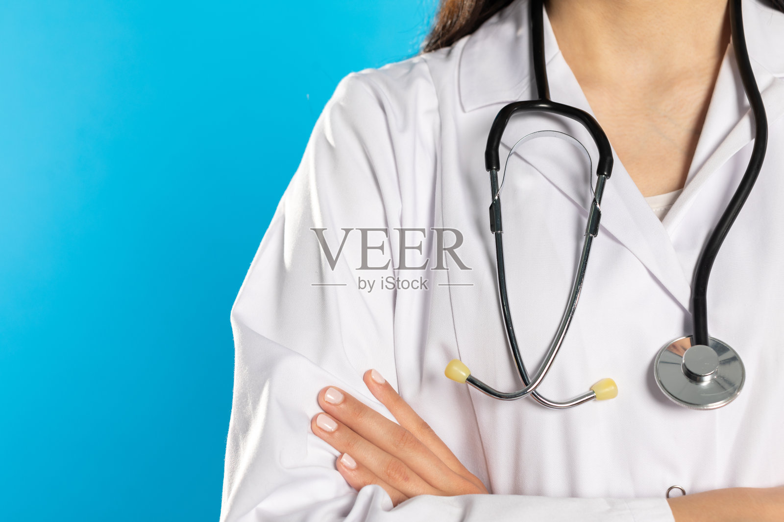 女医生双臂交叉,脖子上挂着听诊器。照片摄影图片