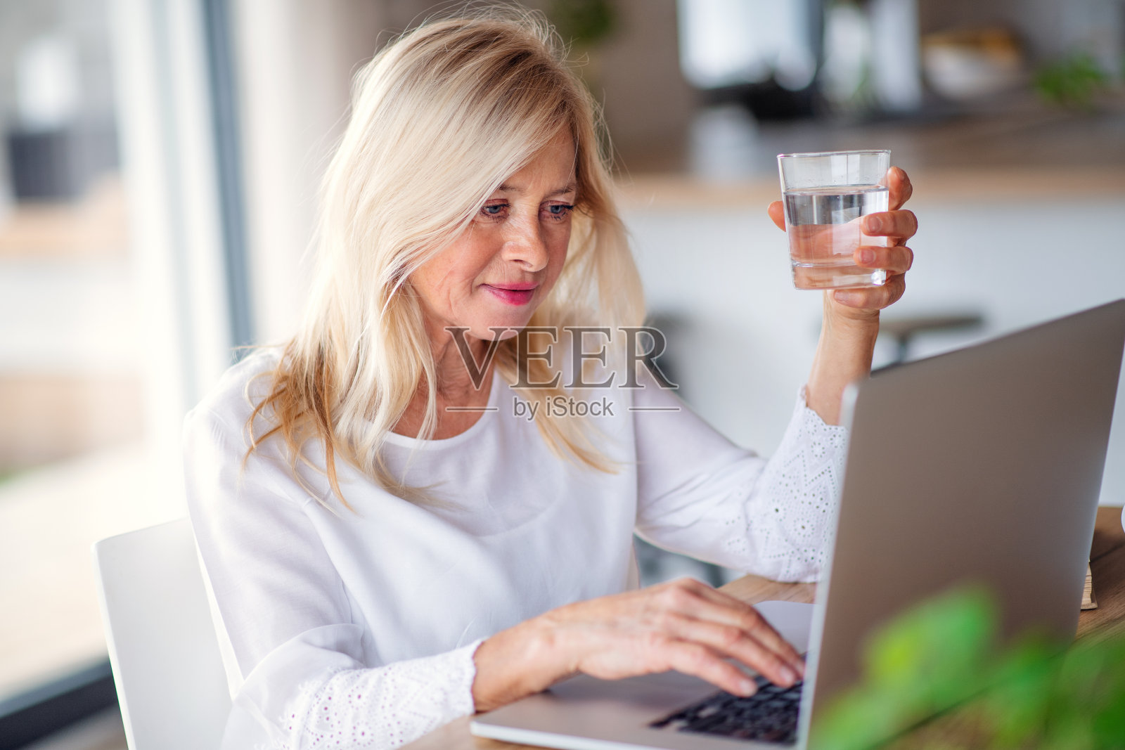 有水和笔记本电脑的资深女性在家办公,工作。照片摄影图片