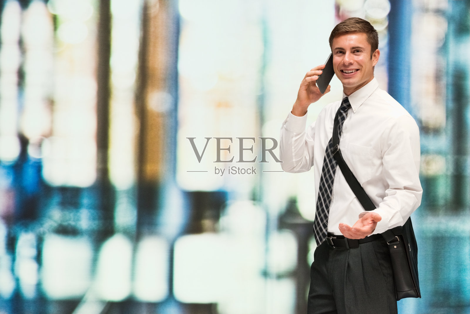 背景散焦的白人男性商务人士,在户外戴肩包,拿着包,使用手机照片摄影图片