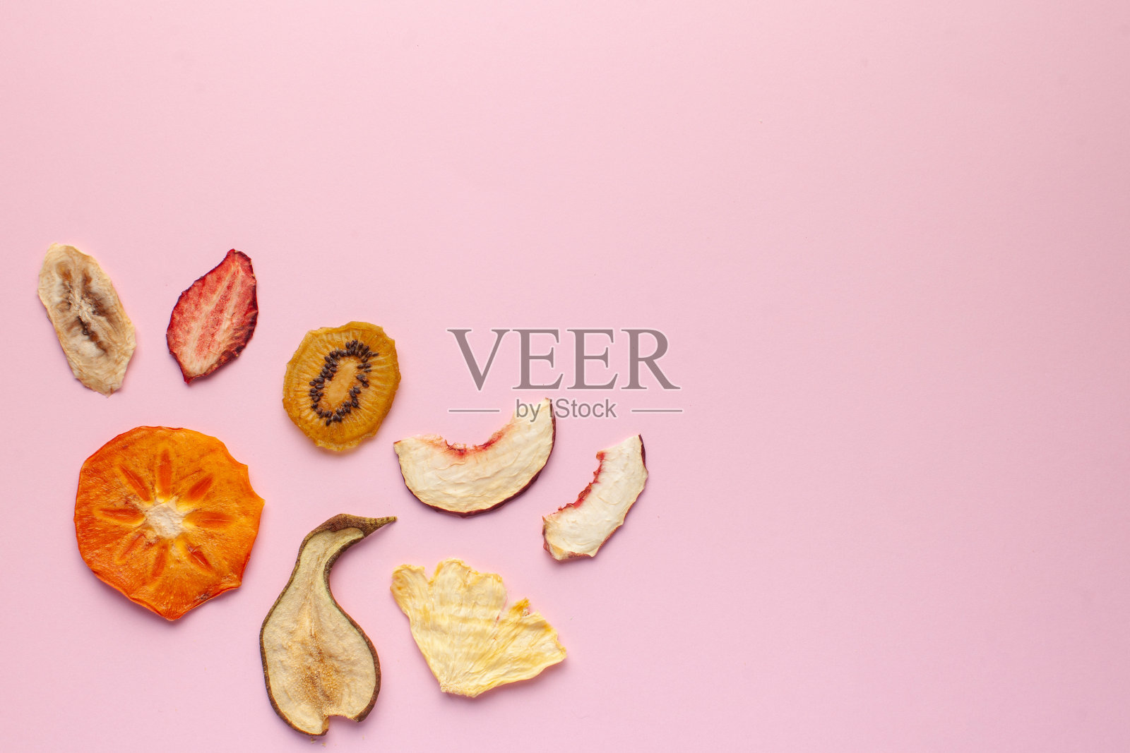 粉红色背景上的干果片。不含糖的健康零食概念,为素食者准备的甜点。副本的空间。照片摄影图片