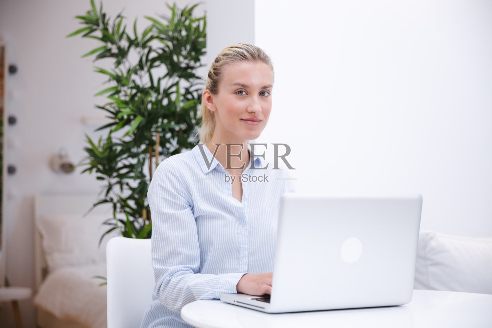 年轻的金发女人在家里用电脑工作。照片摄影图片