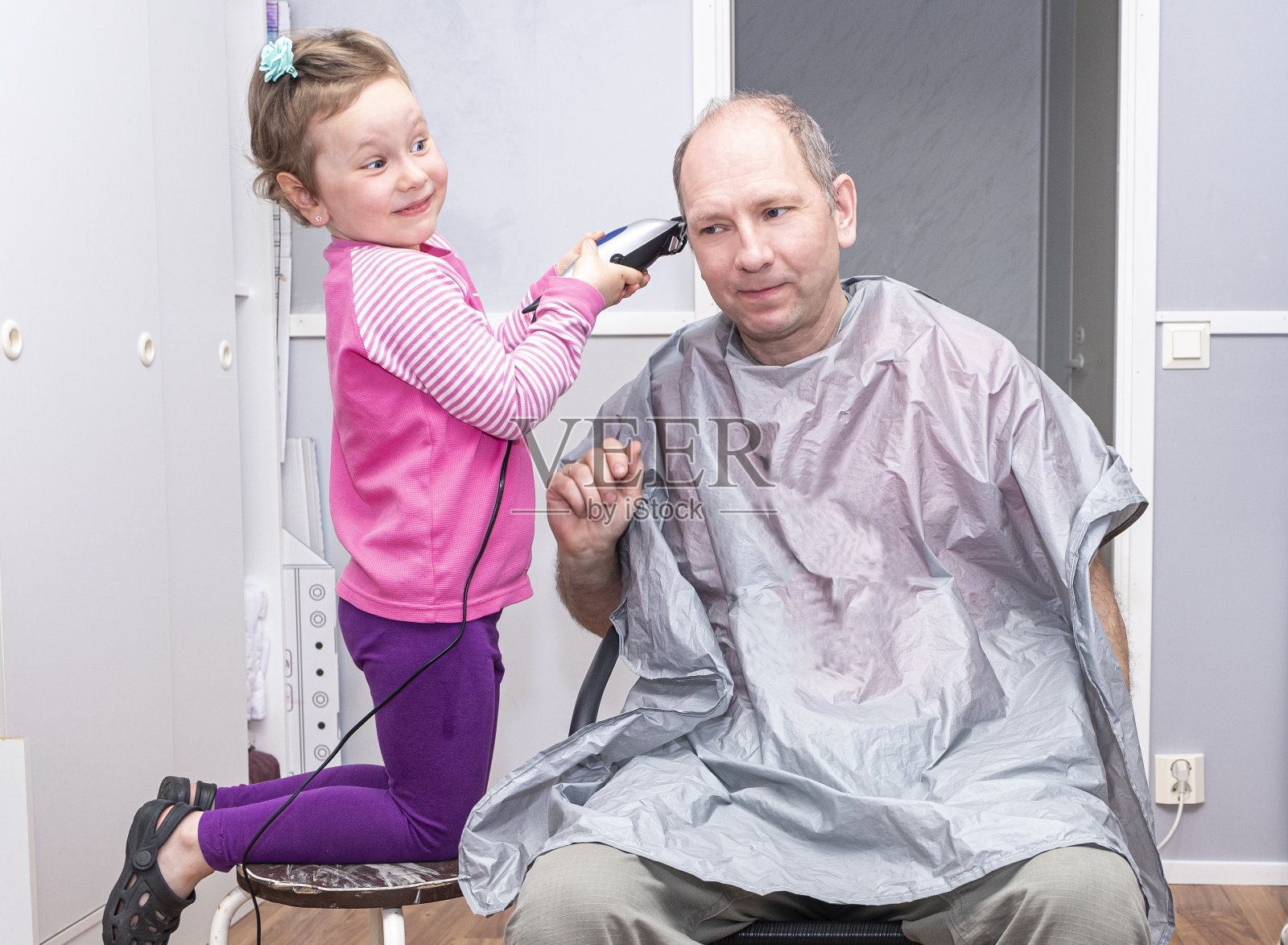 一个5岁的小女孩和她的爸爸在理发店玩,剪着一个理发器。孩子高兴地笑了照片摄影图片