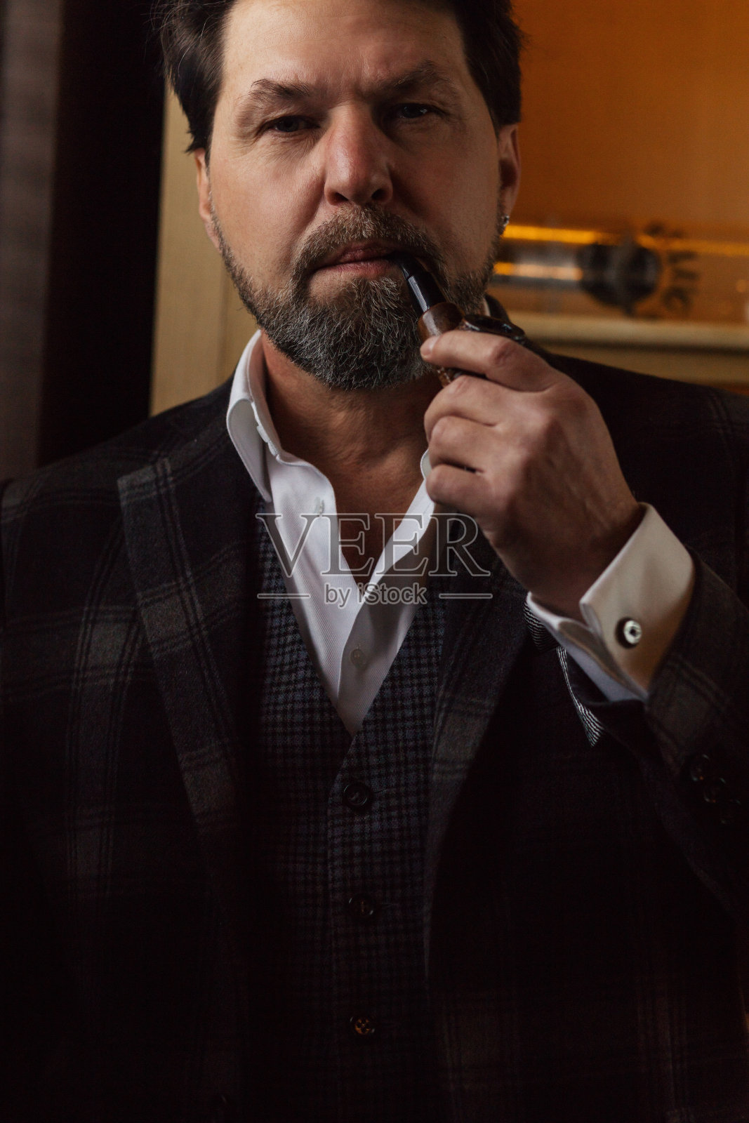 穿着得体,戴着眼镜,抽着烟斗的成熟胡子男人照片摄影图片