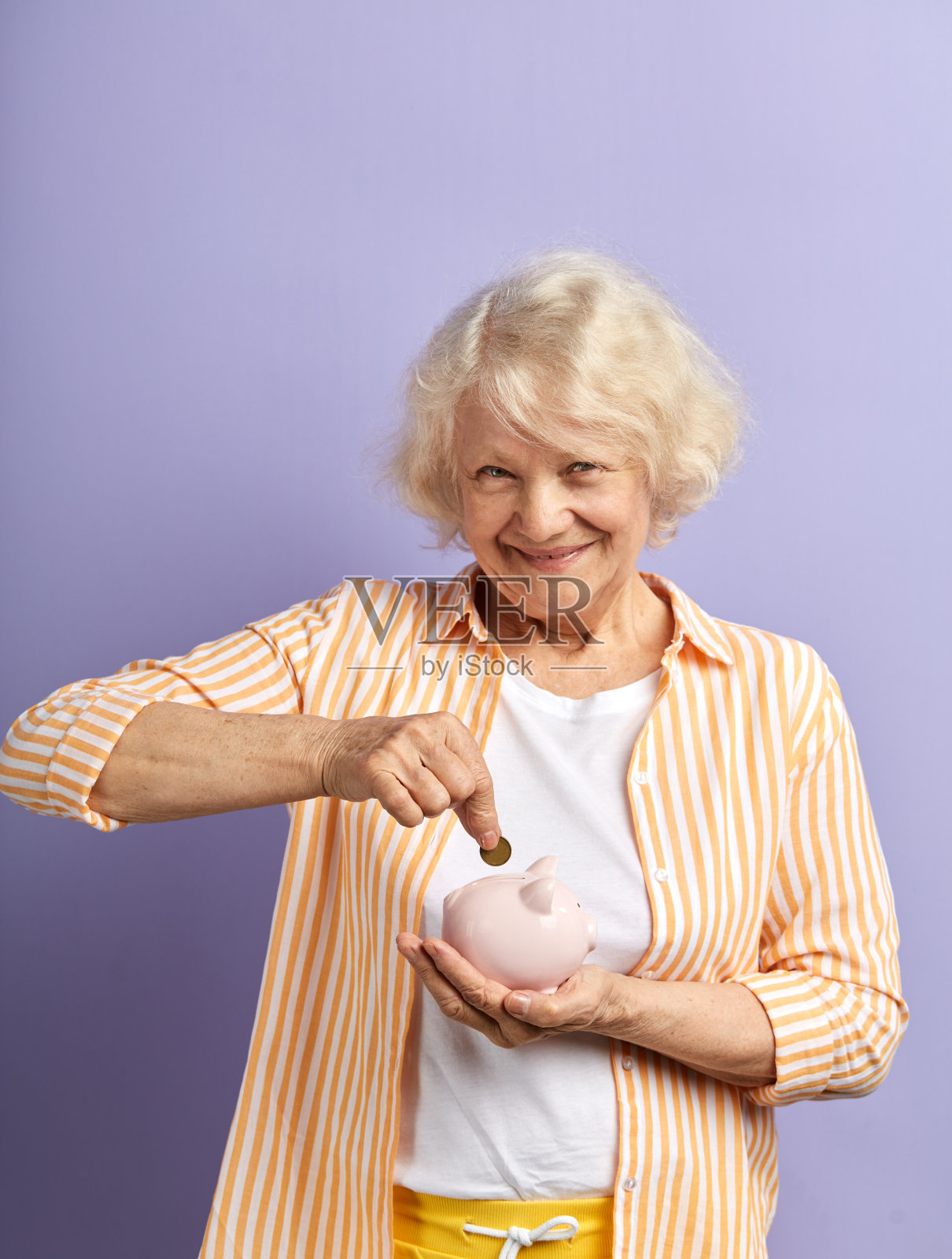 微笑的老妇人将欧元硬币存入储蓄罐,对着镜头微笑照片摄影图片