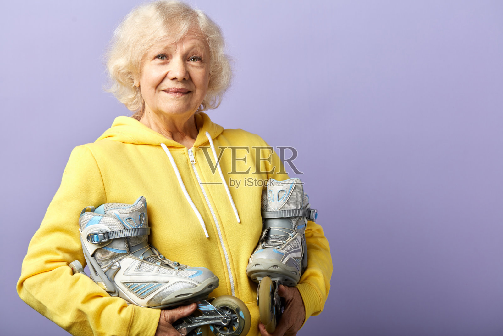 活跃的老年妇女在黄色运动帽衫拿着旱冰鞋摆姿势室内照片摄影图片
