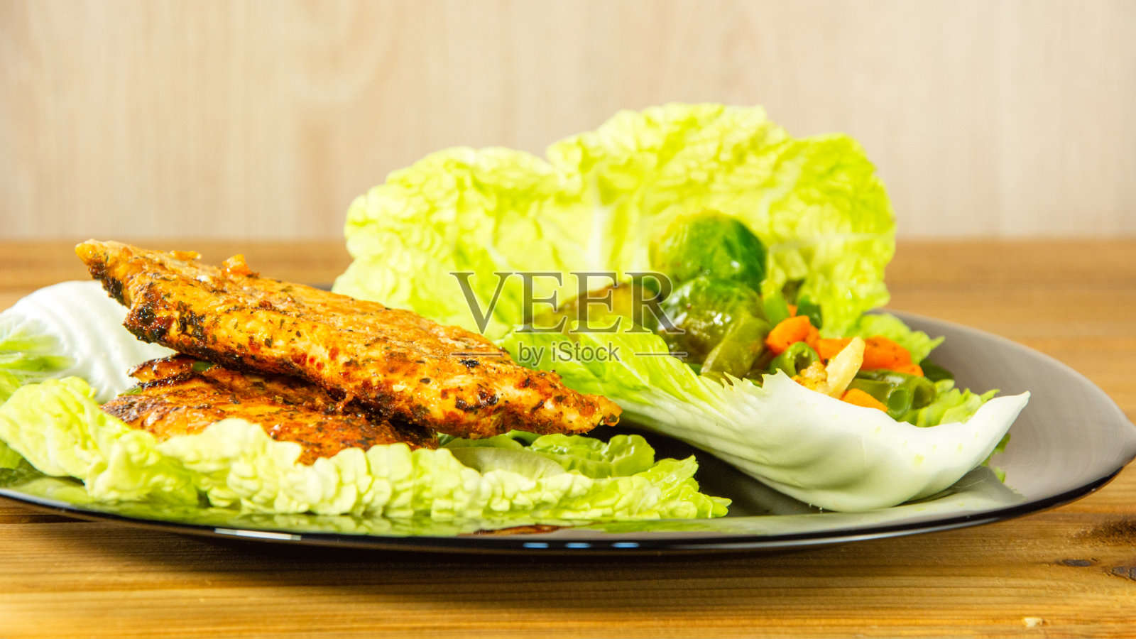 烤鸡胸肉和生菜蔬菜混合物放在一个黑色的盘子里。特写镜头。木头的背景照片摄影图片