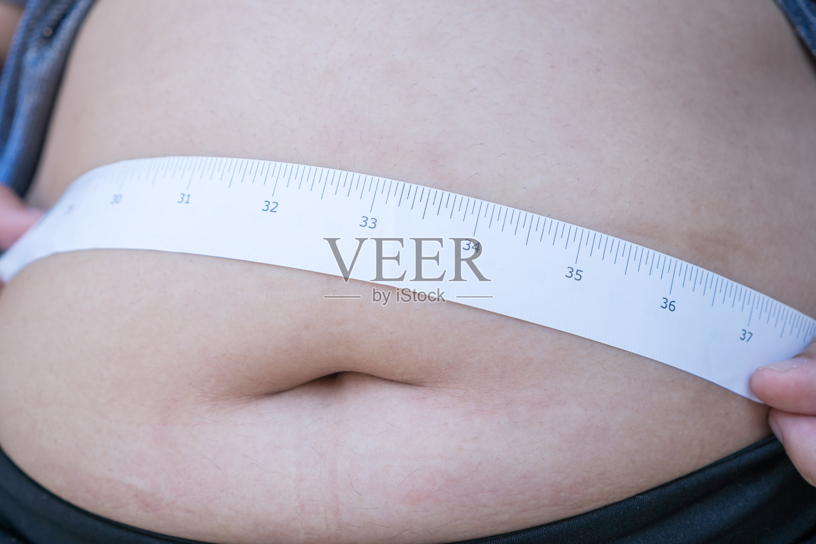 肥胖的亚洲年轻女子用卷尺量她的肚子,穿运动服捏大,有暴饮暴食问题,肥胖。身体脂肪超过最佳水平的人的体重指数(BMI)照片摄影图片