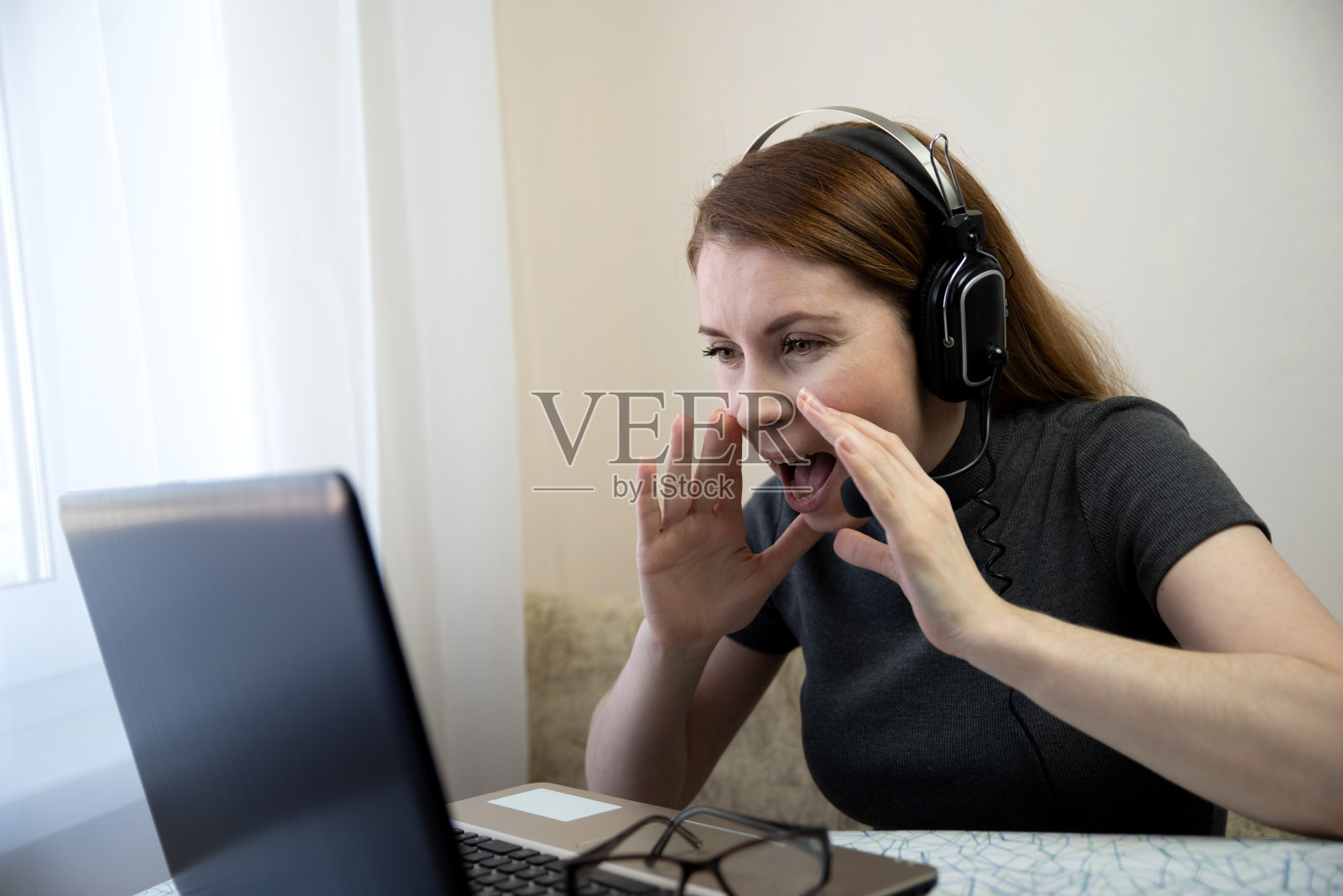 年轻的女商人坐在电脑上,看着屏幕上的视频通话尖叫着,试图分享或讲述一些事情。业务,自由职业的概念。白天靠近窗户的室内拍摄照片摄影图片