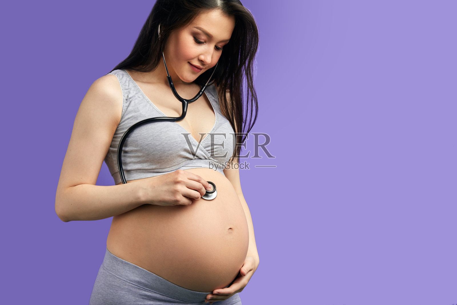 微笑的孕妇使用听诊器听她的腹部照片摄影图片