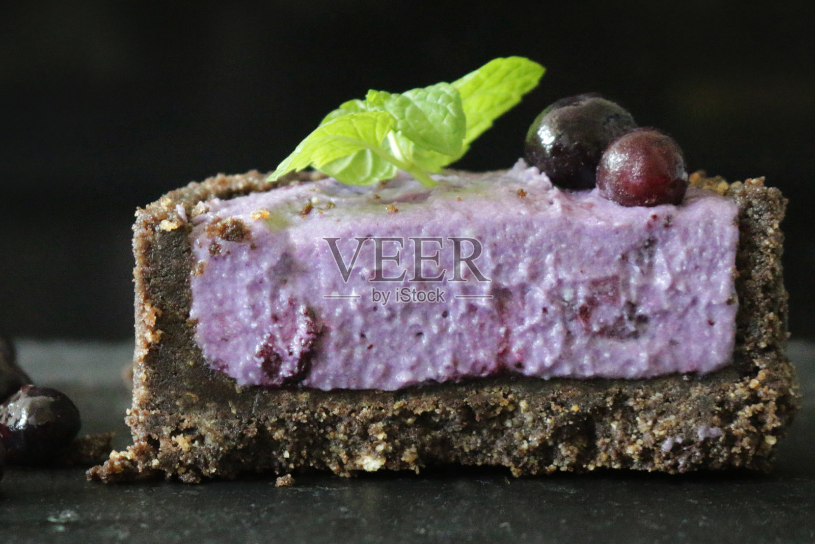 这是一个微型蓝莓芝士蛋糕的特写,在黑色的背景下,奶油饼干的底部环绕着浆果,半块蓝莓马斯卡邦奶油芝士甜点布丁,上面点缀着新鲜的蓝莓和薄荷叶装饰照片摄影图片