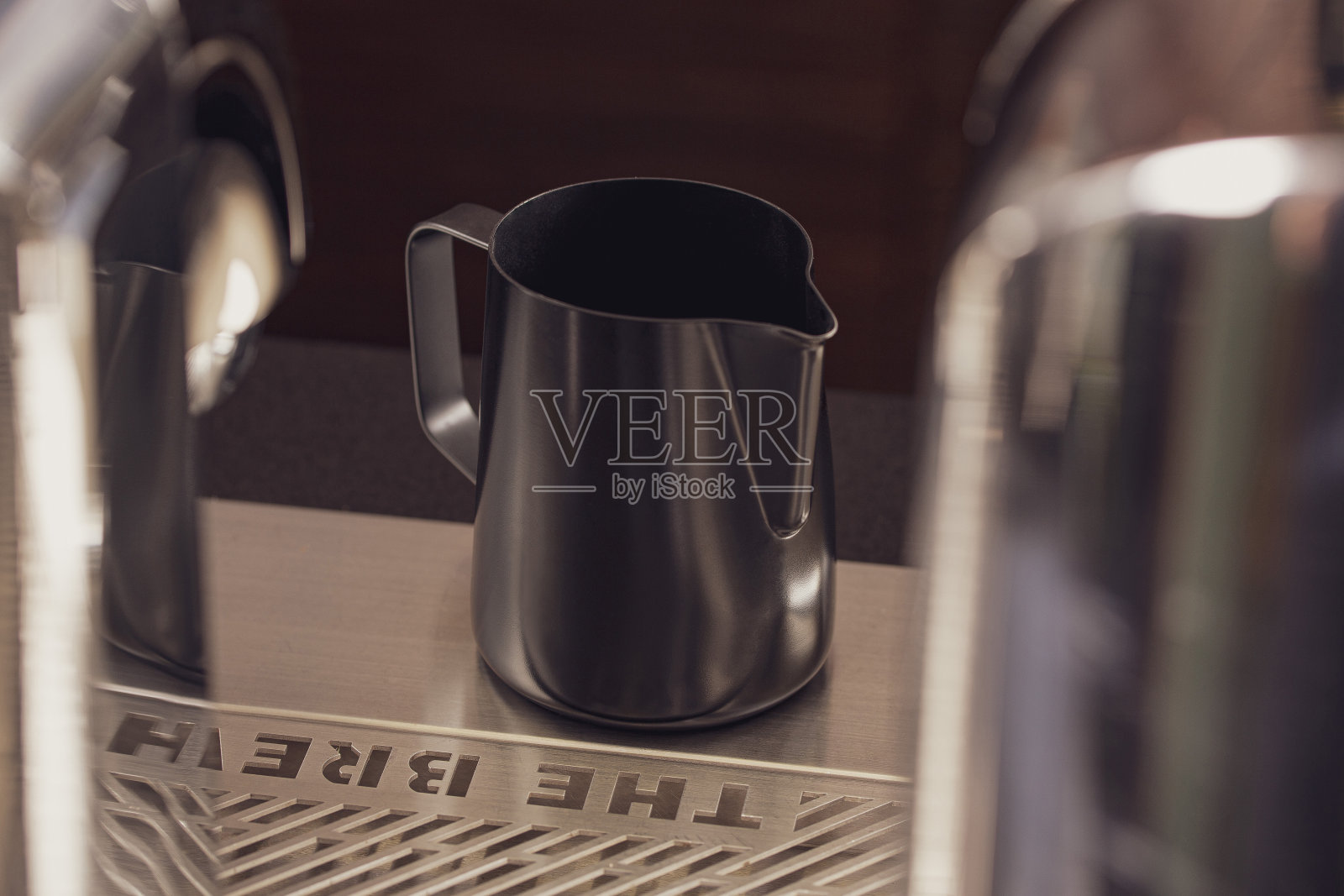 经典的哑光表面不锈钢牛奶泡沫壶杯,带把手,放在桌上。厨房用具,耐热耐用。照片摄影图片