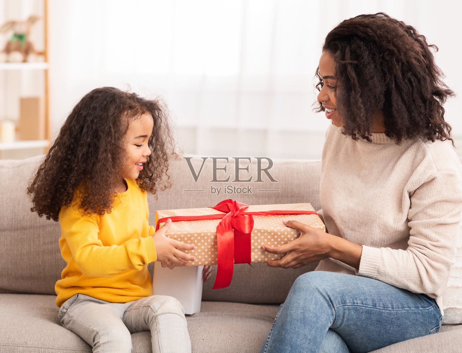 非洲母亲给坐在沙发上的女儿送礼物照片摄影图片