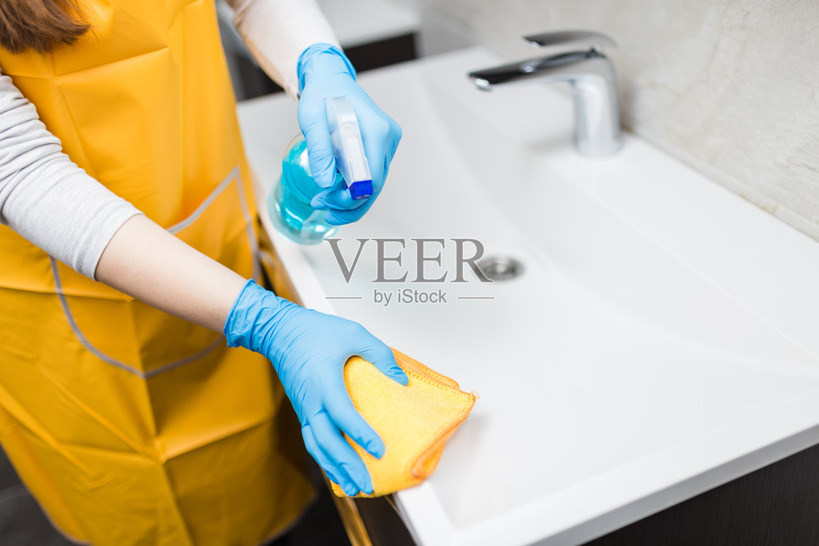 女性双手戴橡胶手套,用喷雾消毒剂和超细纤维布清洁浴室洗手盆边缘。卫生抗菌的概念。照片摄影图片