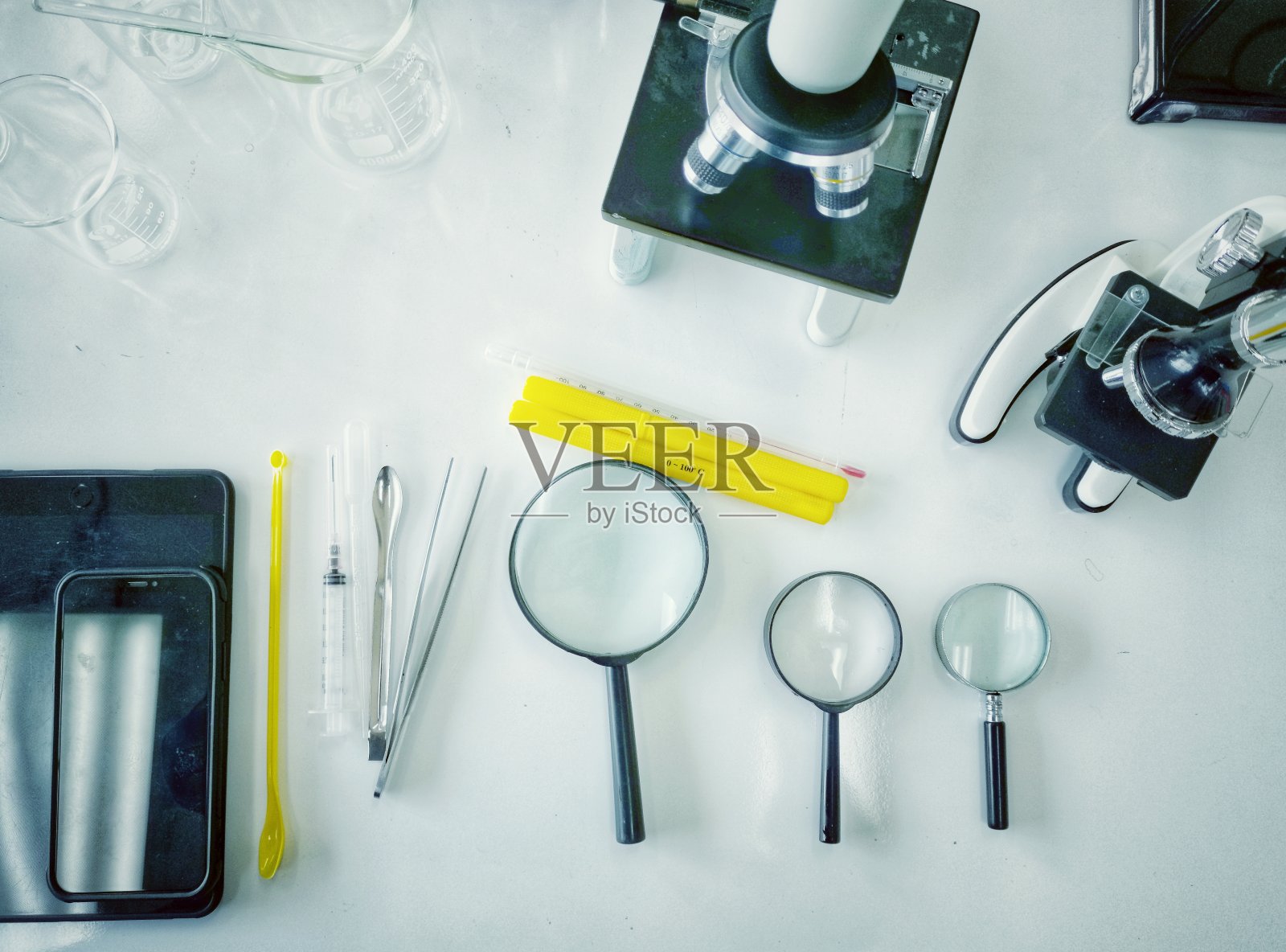 科学桌上的俯视图,显微镜,放大镜,药片,口罩和科学实验室的手机。照片摄影图片