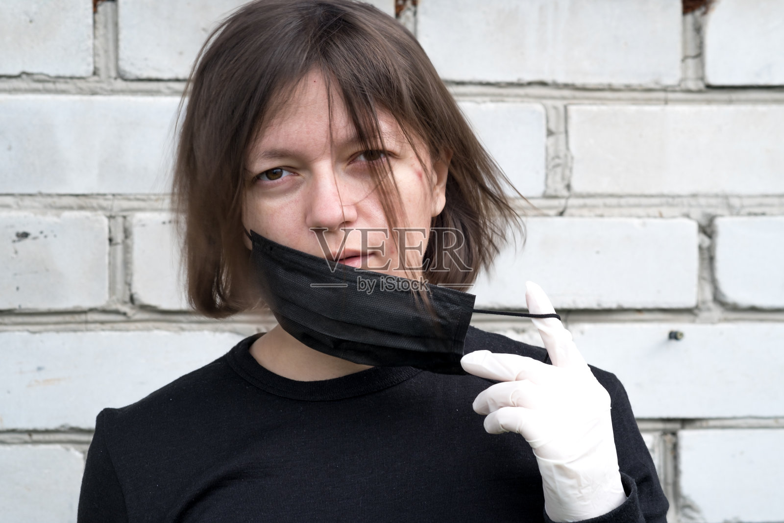 一名小女孩在一堵砖墙后面摘下防止冠状病毒传播的口罩。妇女在隔离和隔离的时候就在大街上照片摄影图片