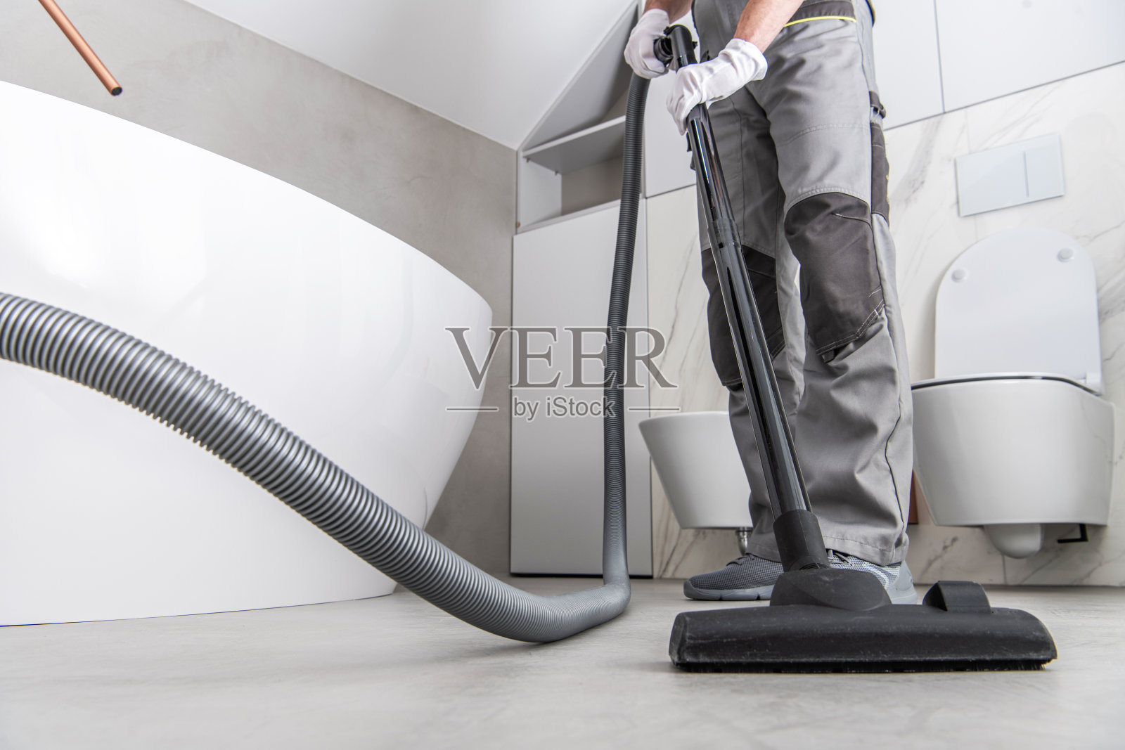 男子吸尘白色瓷砖地板在浴室。照片摄影图片